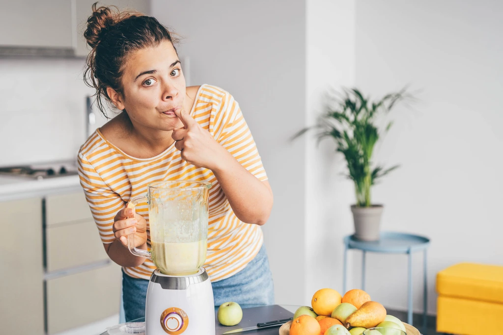 Ava Sinclair playfully tasting a freshly made smoothie from the blender, checking the flavor of her recipe.