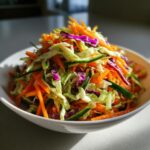 A close-up of a vibrant, freshly tossed cabbage salad featuring shredded carrots, green cabbage, and purple cabbage.