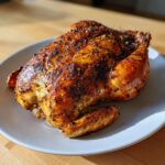 A perfectly cooked, golden-brown air fryer whole chicken with crispy, seasoned skin resting on a light gray plate.