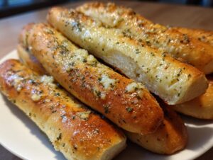 A close-up shot of several golden brown, freshly baked breadsticks topped with melted garlic butter and herbs.