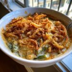 A close-up shot of creamy green bean casserole topped with crispy fried onions, served in a white bowl.