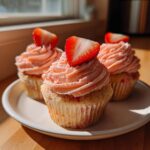 Three delicious strawberry cupcakes with pink frosting and fresh strawberry slices on top, displayed on a white plate.