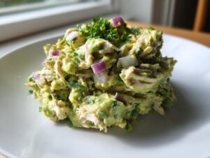 A mound of creamy avocado chicken salad mixed with visible chunks of red onion and topped with fresh parsley.