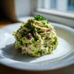 A mound of creamy avocado chicken salad mixed with shredded chicken and diced red onion, garnished with parsley.
