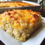 A close-up of a serving of cheesy chicken and rice casserole topped with melted, browned cheddar cheese.