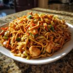 A heaping plate of savory chicken chow mein recipe noodles mixed with chicken pieces, shredded cabbage, and carrots.