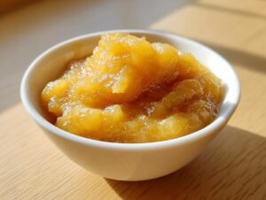 Close-up of chunky, golden homemade applesauce served in a small white bowl on a wooden surface.