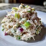 A mound of creamy cottage cheese chicken salad mixed with visible chunks of green celery and purple red onion on a white plate.