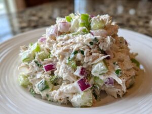 A mound of creamy cottage cheese chicken salad featuring shredded chicken, diced celery, and red onion served on a white plate.