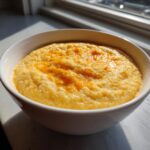 Close-up of a white bowl filled with creamy, yellow cheese grits topped with melted cheddar cheese.