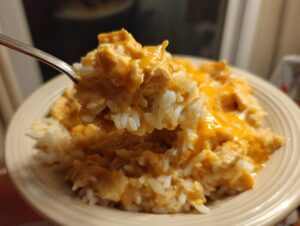 A spoonful of creamy crock pot chicken and rice topped with melted cheddar cheese being lifted from a plate.