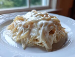 Close-up of fettuccine pasta generously coated in rich, creamy Olive Garden Alfredo Sauce on a white plate.
