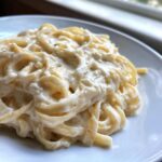 Close-up of fettuccine pasta generously coated in rich, creamy Olive Garden Alfredo Sauce on a white plate.