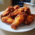 A pile of golden brown, perfectly seasoned crispy air fryer chicken wings stacked on a white plate.