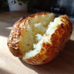 Close-up of a perfectly cooked air fryer baked potato split open to show the fluffy white interior and crispy skin.