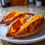 Two fluffy baked sweet potato halves seasoned generously with flaky salt and pepper.