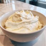 A close-up of perfectly whipped, fluffy cream cheese frosting piled high in a white bowl.