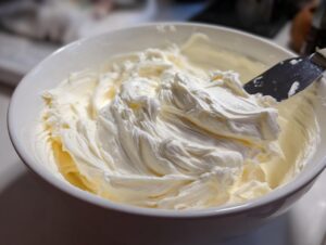 Close-up of smooth, fluffy cream cheese frosting being mixed in a white bowl with an offset spatula.