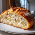 Close-up of a freshly baked sourdough sandwich bread loaf cut in half, showing a light, airy crumb structure.