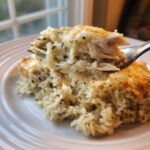 Close-up of a fork lifting a bite of creamy crock pot chicken and rice topped with melted cheese.