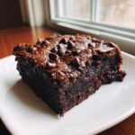 A close-up of a rich, fudgy slice of sweet potato brownies topped with chocolate chips on a white plate.