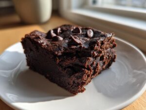 A close-up, decadent square of sweet potato brownies topped with melted chocolate chips, sitting on a white plate.