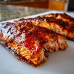 Close-up of a perfectly cooked, glazed salmon fillet showing flaky texture and rich, dark seasoning.
