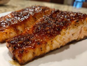 Close-up of two perfectly cooked salmon fillets with a thick, glossy, dark brown glaze and visible seasoning.
