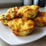 A close-up of several golden brown, fluffy homemade egg bites stacked on a white plate.