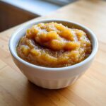 Close-up of chunky, spiced homemade applesauce served in a small white ramekin on a wooden surface.