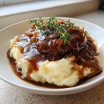 Rich homemade brown gravy with caramelized onions poured over mashed potatoes and meatloaf, garnished with fresh thyme.