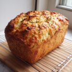A golden brown loaf of Italian herb and cheese bread cooling on a wire rack.