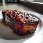 A thick, beautifully glazed and caramelized piece of pork steak resting on a white plate.