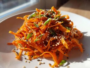 Close-up of a bright orange raw carrot salad, shredded and topped with sesame seeds and green onions.