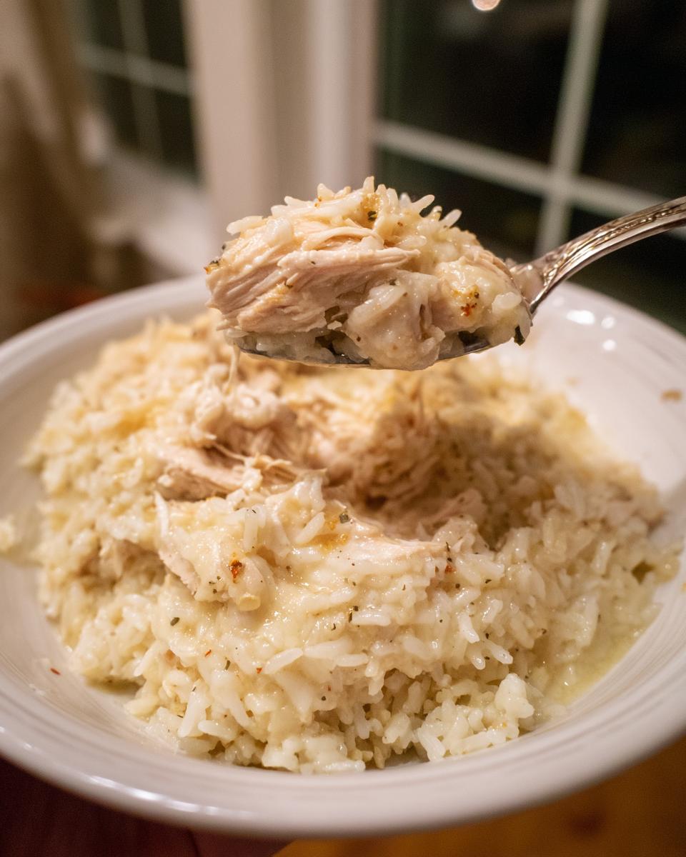 A spoonful of creamy crock pot chicken and rice being lifted from a white bowl.