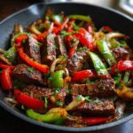 Close-up of sizzling steak fajitas with sliced steak, red and green bell peppers, and onions in a cast iron skillet.