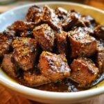 Close-up of tender, cubed crockpot steak coated in a rich, dark sauce with visible pepper flakes.