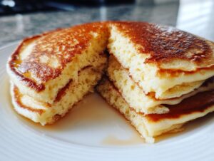 Close-up of a stack of fluffy pancakes cut in half, revealing the airy interior and drizzled with syrup.