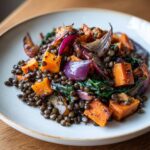 Close-up of a hearty veggie lentil salad featuring dark lentils, roasted orange sweet potato chunks, and vibrant red onion wedges.