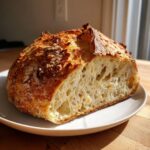A freshly baked loaf of artisan bread, sliced in half to show the open, airy crumb structure.