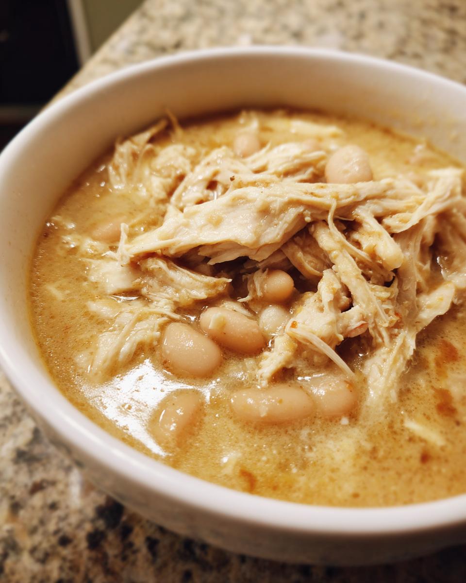 A close-up view of a hearty bowl of white chicken chili, featuring shredded white chicken and cannellini beans in a creamy broth.