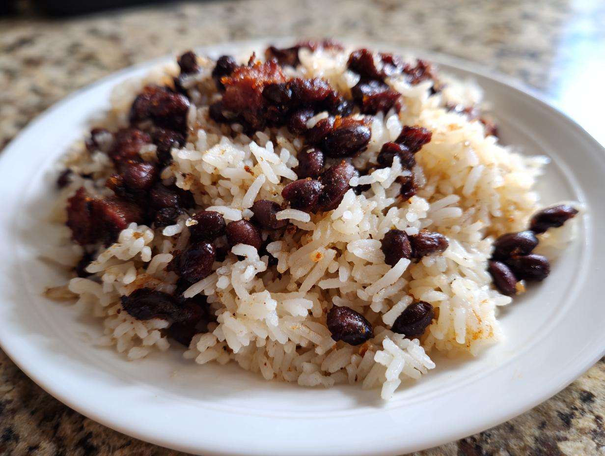 A close-up of a serving of fluffy white rice mixed with dark, seasoned black beans and rice on a white plate.