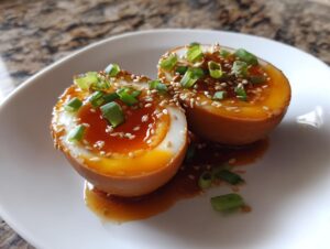 Two halves of a soft-boiled marinated eggs, showing gooey orange yolks, topped with sesame seeds and chopped green onions.
