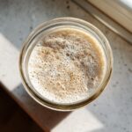 Overhead view of an active sourdough starter in a glass jar, showing a thick layer of bubbles on top.