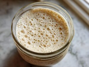 Overhead view of a very active sourdough starter, showing a thick layer of small, tan-colored bubbles.