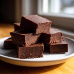 A stack of rich, dark chocolate fudge squares piled high on a white plate, ready to eat.