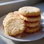 A stack and pile of freshly baked, golden butter cookies generously coated in sparkling sugar crystals.