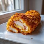 Close-up of a perfectly cooked chicken cordon bleu roll showing melted cheese and ham inside the crispy breading.