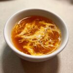 A white bowl filled with hot, savory broth featuring delicate ribbons of cooked egg drop soup.