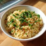 A white bowl filled with perfectly cooked, fluffy rice pilaf garnished generously with chopped fresh parsley.